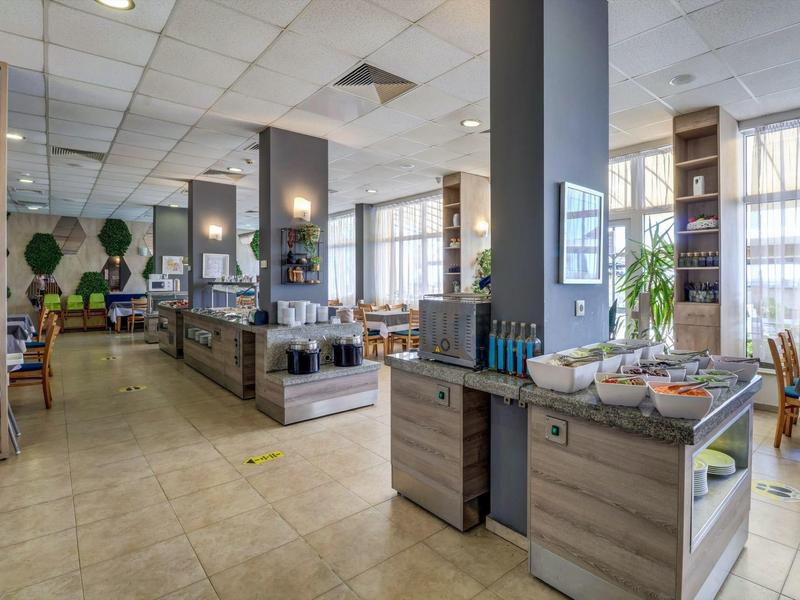 Moderner Gastraum mit hellen Wänden, großen Fenstern, Holz- und Steinelementen, Buffet und Stühlen.