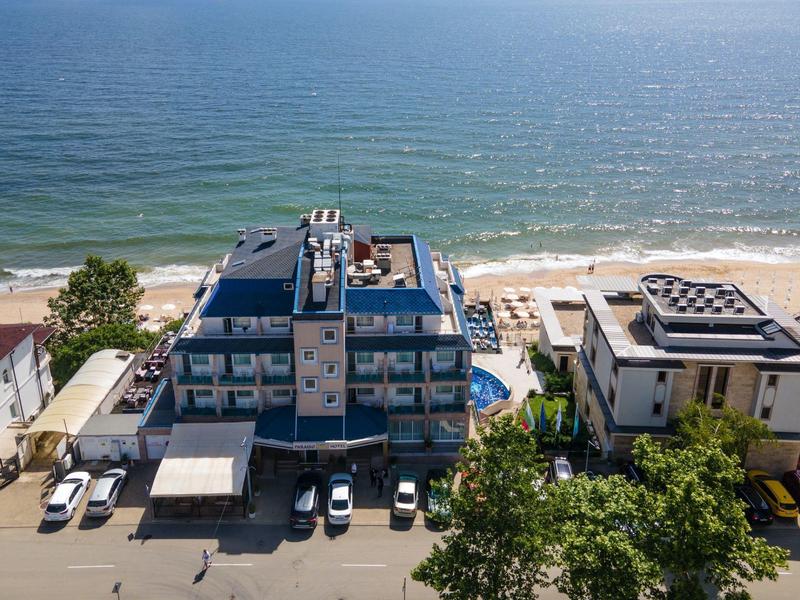 Blick auf moderne Wohngebäude am Strand mit geparkten Autos und grünem Baumbestand.
