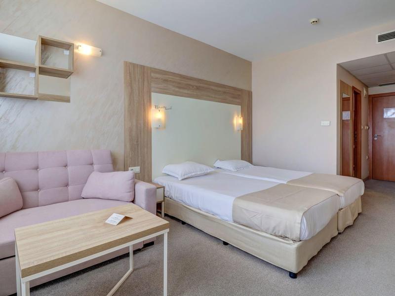 Modernes Hotelzimmer mit zwei Betten, Sofa, Holztisch und minimalistischer Wanddekoration.