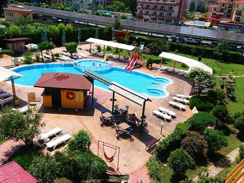 Freizeitbad mit Pool, Liegestühlen, Rutschen, Sonnenschirmen und grünen Pflanzen umsäumt.