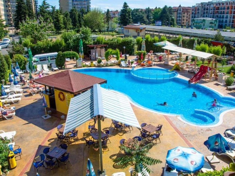 Großer Pool mit blauer Wasserfläche, umgeben von Liegestühlen, Sonnenschirmen und grünen Pflanzen.