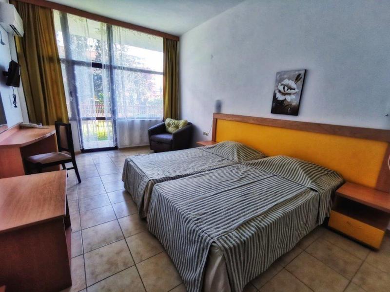 Helles Hotelzimmer mit Doppelbett, grauer Bettdecke, Schreibtisch und Balkon mit Glasfenster.