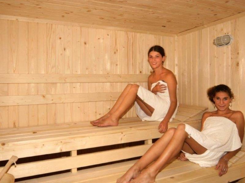 Zwei Frauen in weißen Handtüchern sitzen in einer hellen Holzsauna auf Bänken.