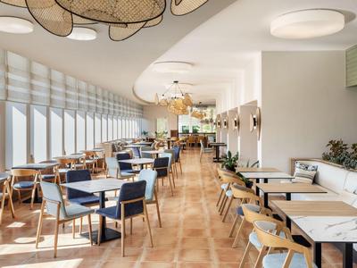 Heller Hotelrestaurant mit großen Fenstern, Holzstühlen und modernen Tischen