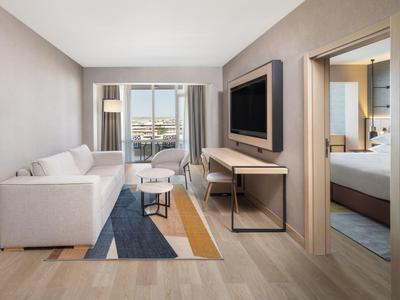 Modern hotel room with sofa, TV, rug, and view into the bedroom.