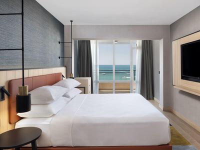 Modern hotel room with large bed, balcony, and sea view.