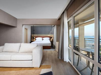 Modern hotel room with comfortable sofa, bed, and large window overlooking the sea.