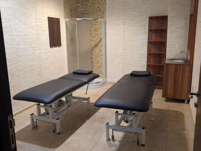 Behandlungsraum mit zwei Massageliegen und Dusche in modernem, neutralem Stil.