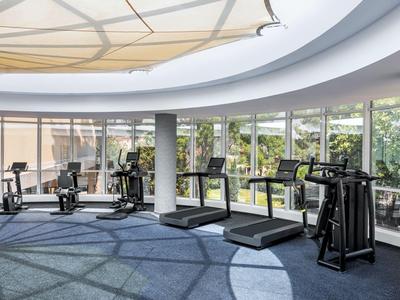 Moderner Fitnessraum mit Laufbändern und Trainingsgeräten in einem Hotel mit großen Fenstern.