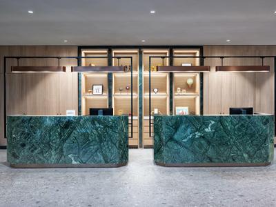 Modern hotel lobby reception with two green marble counters and wooden wall in the background.