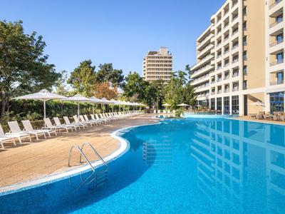 Großer Außenpool mit Liegestühlen und Hotelgebäuden bei sonnigem Wetter.