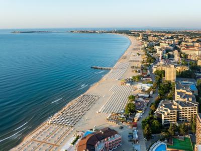 Aerial view of a long sandy beach with umbrellas and hotels along the shore.