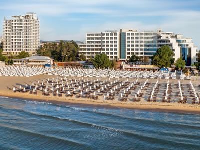 Beach with numerous sun loungers in front of several hotels under clear sky.