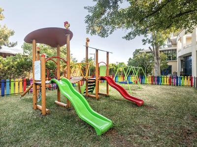Colorful playground with slides and swings on grass in a hotel garden.