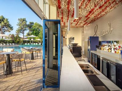 Moderner Außenbereich mit Bar und Swimmingpool, umgeben von Tischen und Sonnenschirmen.