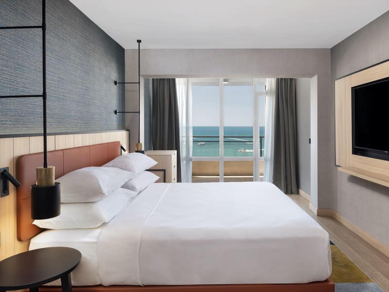 Modern hotel room with large bed, balcony, and sea view.