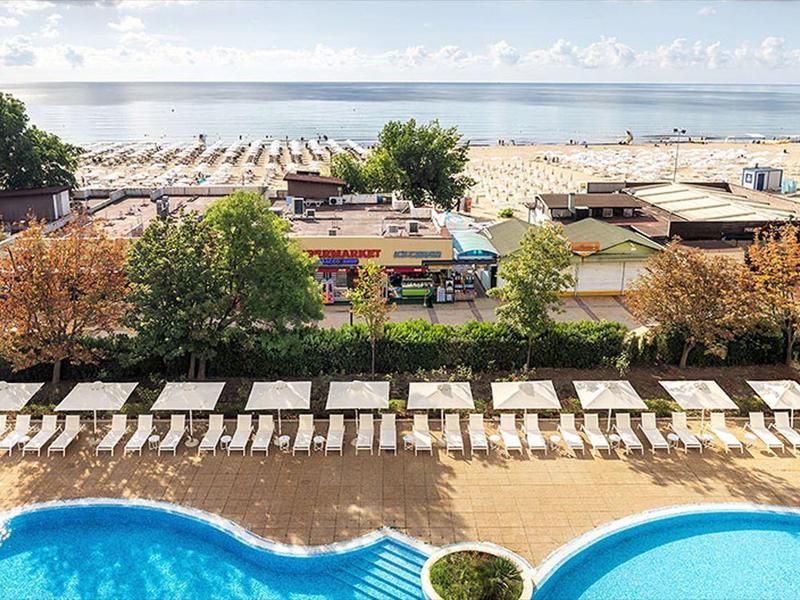 View of pool with sun loungers and beach with umbrellas by the sea in the background.