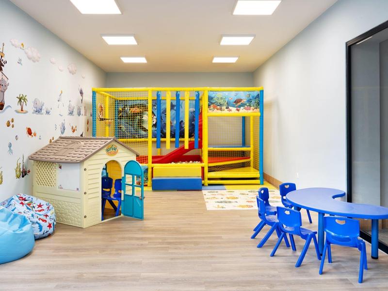 Colorful children's play area with climbing frame, playhouse, tables, and beanbags in a room.