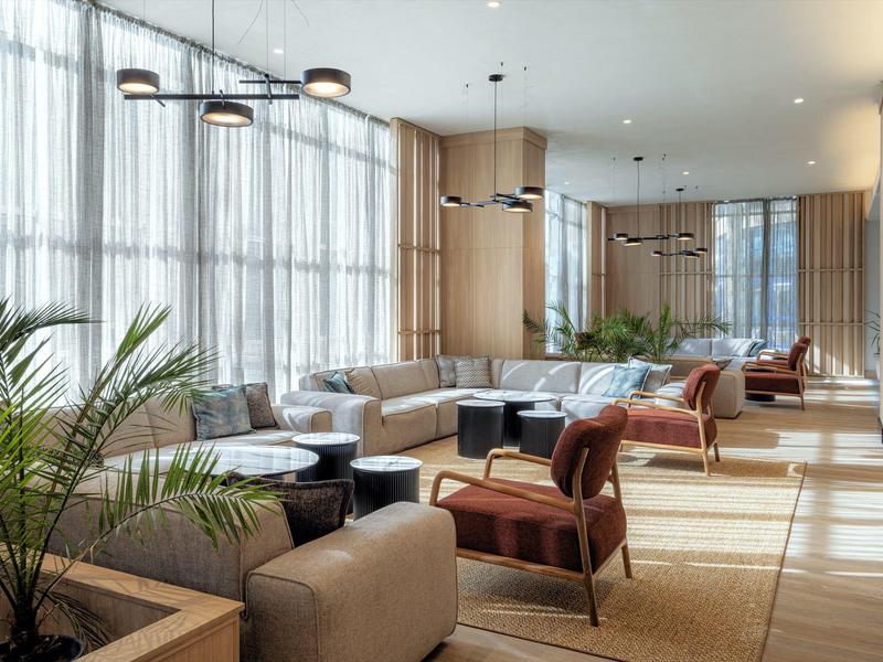 Bright modern lounge area with large windows, armchairs, and plants in a hotel.