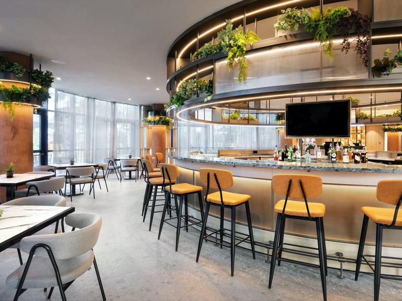 Modern hotel bar area with stylish counter, bar stools, and large windows with outdoor view.