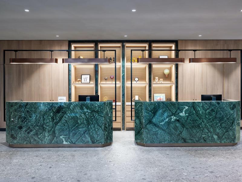 Modern hotel lobby reception with two green marble counters and wooden wall in the background.