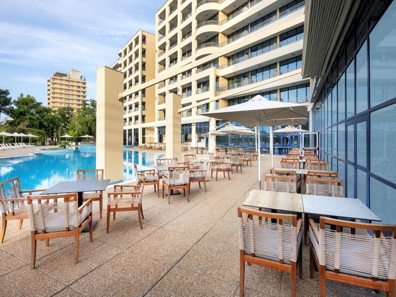 Terrace with tables and chairs beside a swimming pool at a modern hotel building.