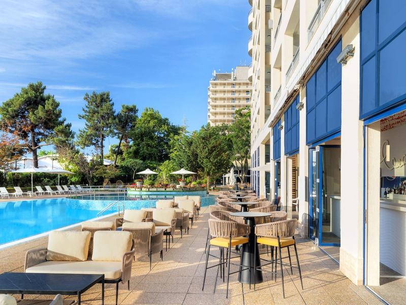 Outdoor hotel area with swimming pool, tables, and chairs under a blue sky.
