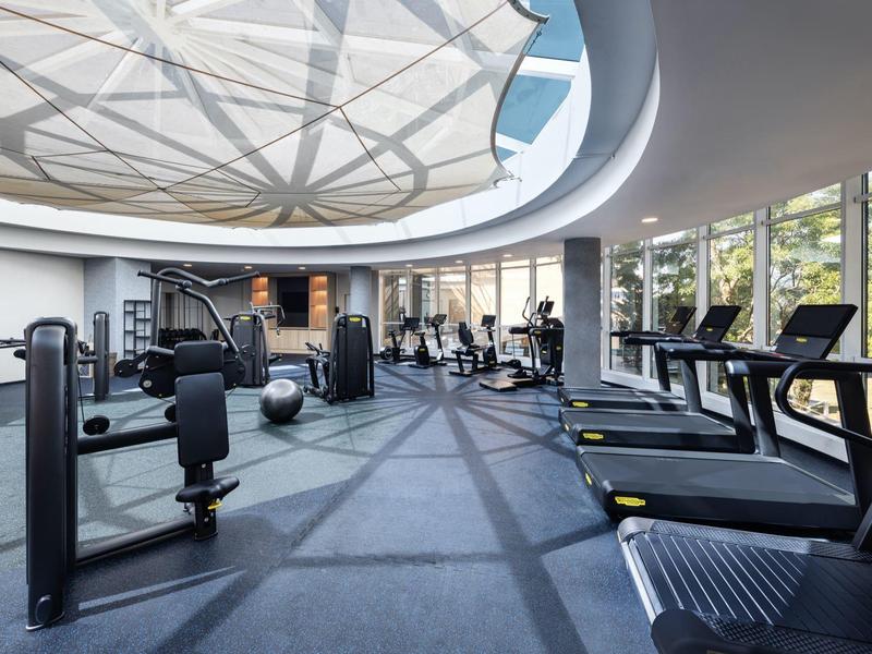 Modern gym with treadmills and fitness equipment under a large circular skylight.