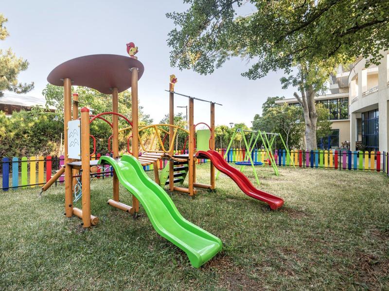 Colorful playground with slides and swings on grass in a hotel garden.