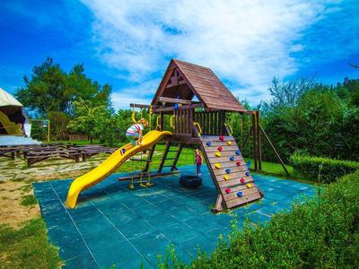 Bunter Kinderspielplatz mit Rutsche, Kletterwand und Schaukel unter blauem Himmel.