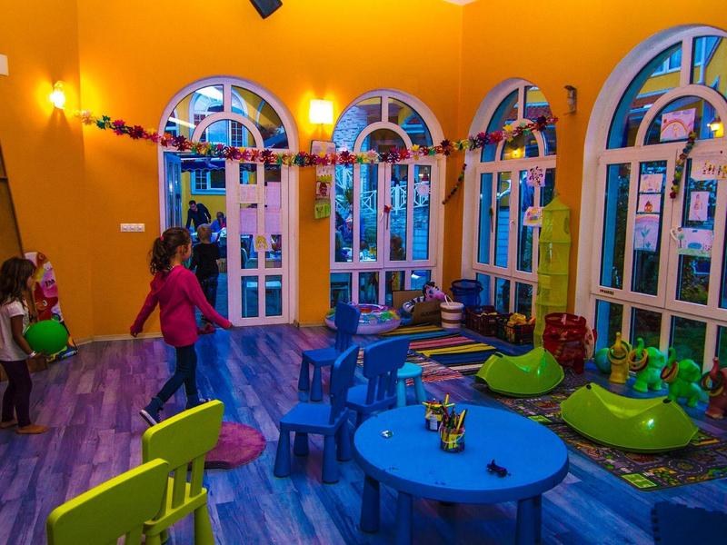 Buntes Kinderspielzimmer mit großen Fensterbögen, bunten Möbeln und spielenden Kindern.