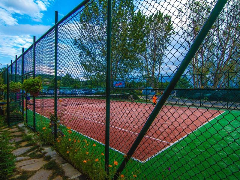 Ein Tennisplatz mit rotem und grünem Belag, umgeben von einem schwarzen Maschendrahtzaun.