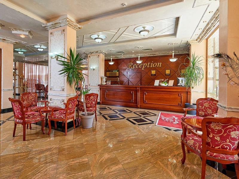 Heller Hotellobby mit Holzempfang, roten Sesseln, Pflanzen und Marmorboden.