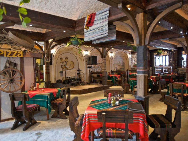 Rustikales Restaurant mit Holzbalken, bunten Tischtüchern und einer Bühne im Hintergrund.