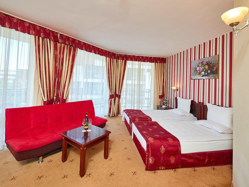 Helles Hotelzimmer mit roten Vorhängen, gestreifter Wand, Doppelbett und rotem Sofa.