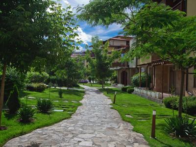 Kręta kamienna ścieżka prowadzi przez zielony ogród obok wielopiętrowego budynku.