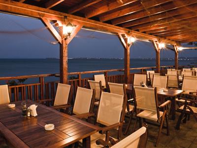 Otwarty taras restauracji z meblami drewnianymi i widokiem na morze o zmierzchu.