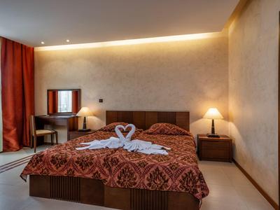 Gezellige hotelkamer met tweepersoonsbed, warm licht en balkon met rode gordijnen.