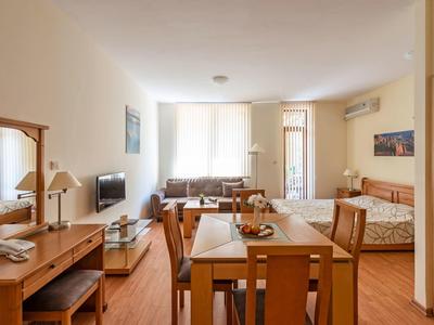 Lichte hotelkamer met eetgedeelte, bank, bed en bureau in warme houttinten.