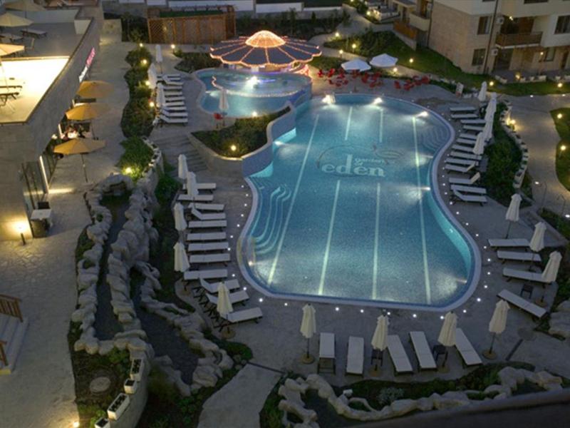 Verlicht hotelzwembad met ligstoelen en parasols ’s nachts.