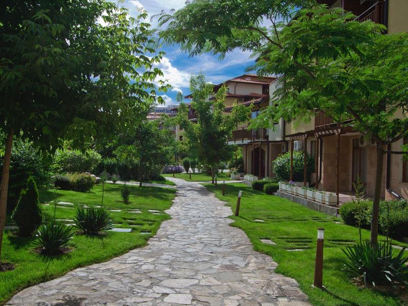 Geplaveid pad loopt door groene tuin met bomen en gebouwen aan beide zijden.