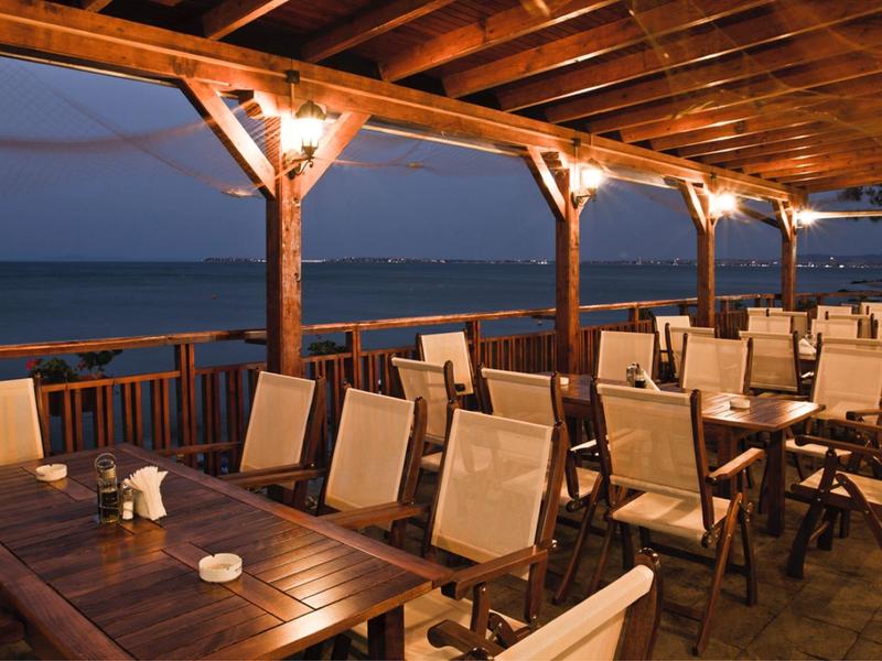 Avonddterras van een strandrestaurant met houten stoelen en tafels onder een overdekte ruimte.