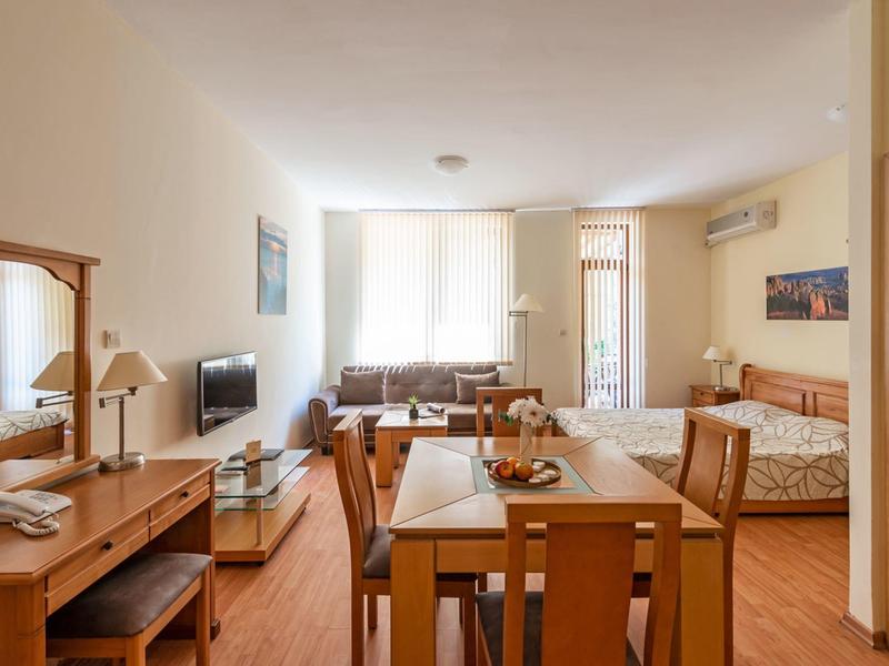 Lichte hotelkamer met eetgedeelte, bank, bed en bureau in warme houttinten.