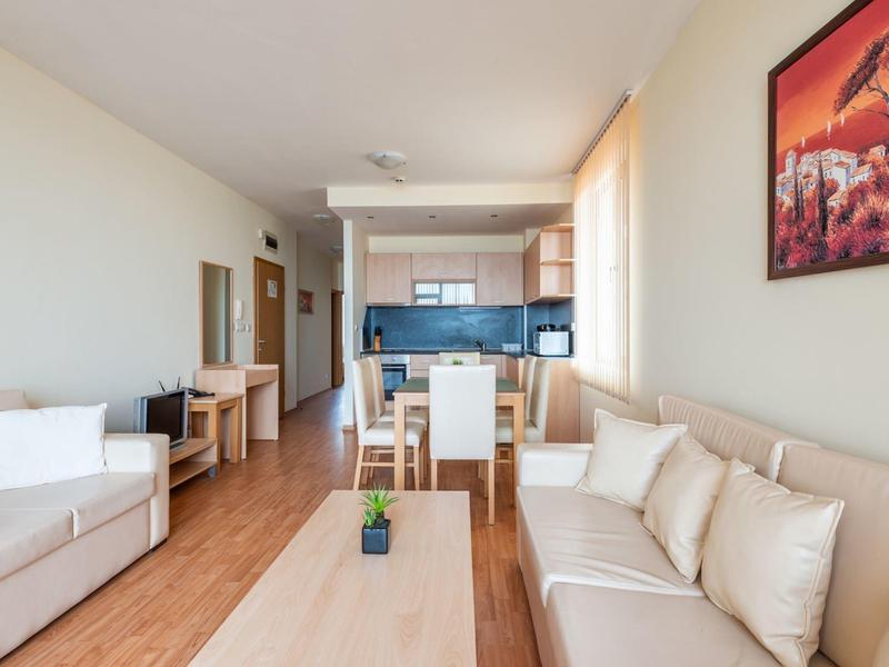 Lichte woonkamer met twee banken, eettafel en moderne kitchenette op de achtergrond.