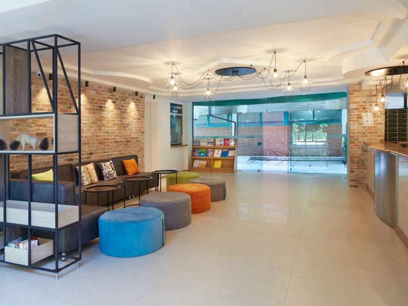 Moderne hotel lobby met zithoek, kleurrijke poefs en groot raamgedeelte.