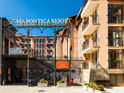 Eingang zum Via Pontica Resort mit Treppen, Balkonen, Blumen und orangefarbenem Hinweisschild.