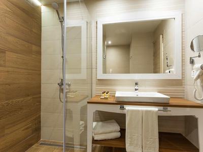 Badezimmer mit Holzpaneelen, Glasdusche, weißem Waschbecken, großem Spiegel und Handtüchern.