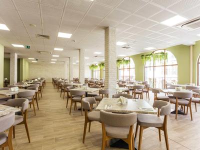 Ristorante luminoso e moderno con molti tavoli, sedie e grandi finestre.