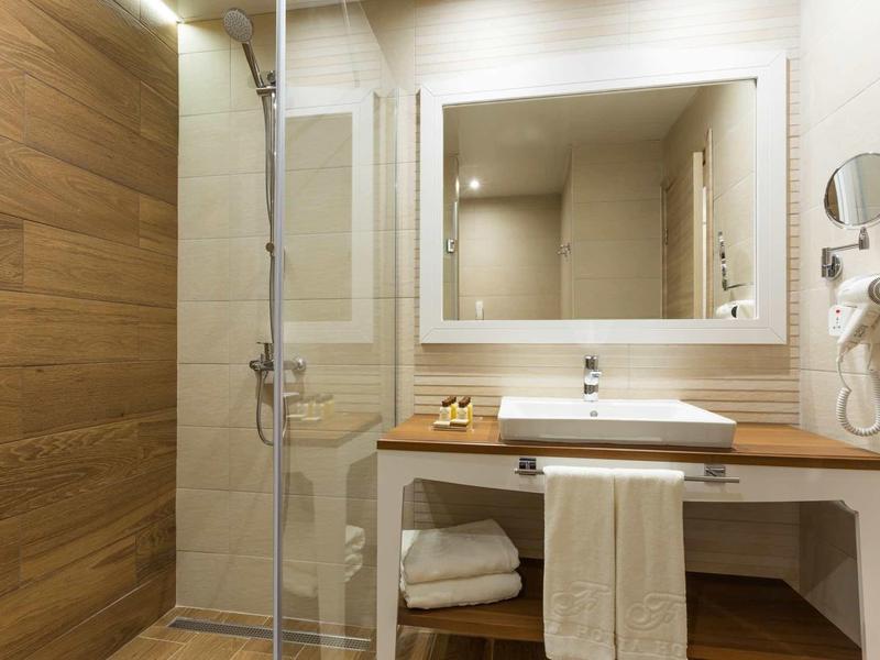 Badezimmer mit Holzpaneelen, Glasdusche, weißem Waschbecken, großem Spiegel und Handtüchern.