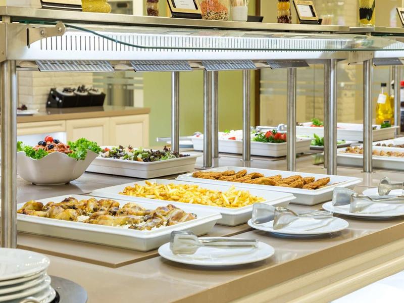 Buffet mit verschiedenem Fingerfood, Salat, Tellern und Besteck auf hellem Holztisch.